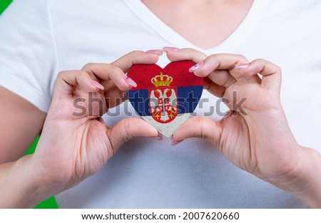Woman in white t-shirt holds a heart in the form flag Serbia on her chest. Photo for a postcard on Flag Day, Independence Day, travel, patriotism, other holiday