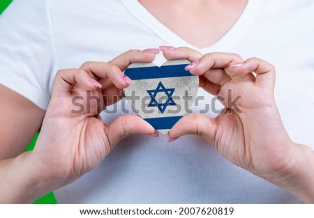 Woman in white t-shirt holds a heart in the form flag Israel on her chest. Photo for a postcard on Flag Day, Independence Day, travel, patriotism, other holiday Royalty-Free Stock Photo #2007620819