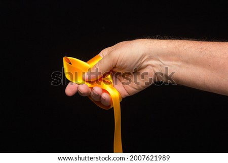 yellow ribbon in the palm of the hand on a black background; preparing the ribbon for wrapping a gift.