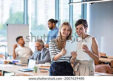 Shot of two businesswomen using a digital tablet together during a collaboration at work.  Female colleagues looking at tablet PC. Business people are working at desk. 