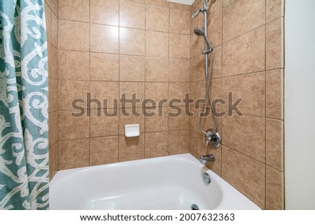 Alcove bathtub with brown ceramic tile surround and patterned shower curtain Royalty-Free Stock Photo #2007632363