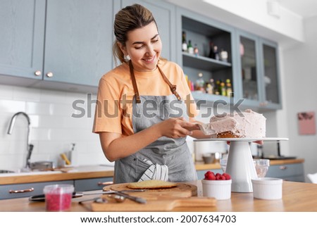 culinary, baking and cooking food concept - happy smiling young woman making layer cake and spreading topping cream on kitchen at home Royalty-Free Stock Photo #2007634703