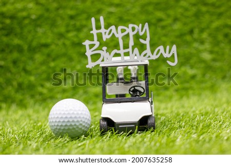 Golf cart is carrying Happy Birthday Sign with golf ball on green grass