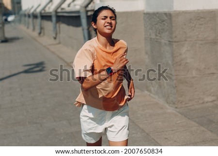 Young indian woman runner jogging in wet sweaty t-shirt at city street. Royalty-Free Stock Photo #2007650834