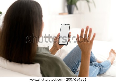 Indian woman holding and using smartphone with black empty screen for video connection, waving hello into webcam, using new mobile app for virtual meeting. Mockup, copy space for advertising