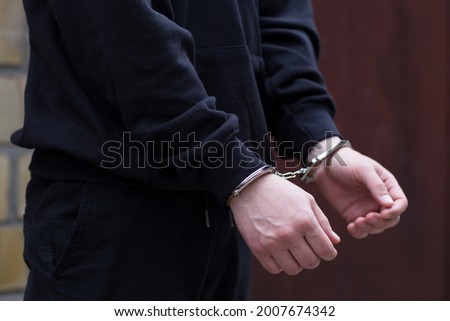 Thief under arrest and get cuffed by policeman Bad person stand against wall, get hand crossed back with handcuffs Murderer is criminal person He can be cyber crime Human trafficking Criminal concept Royalty-Free Stock Photo #2007674342