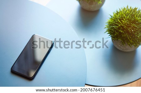 High angle view of blue round tables pair with different height. Green plant and modern smartphone laying on coffee tables. Modern technology, wireless device and transfer of energy concept.
