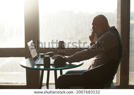 photographer is editing his photo while sitting at a table near the window.