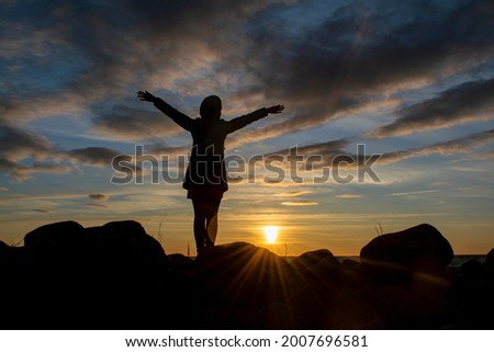 Silhouette of a young girl with hands raised up against the background of the evening sky. World perception concept.