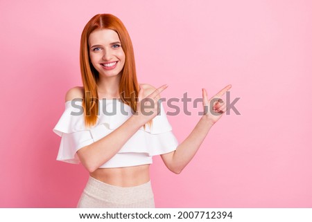 Portrait of attractive cheerful red-haired girl demonstrating copy empty blank space ad isolated over pink pastel color background