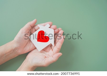 white house paper cut with red heart shape in hands on green background, homeless housing shelter and real estate , family house insurance, social distancing, home isolation concept