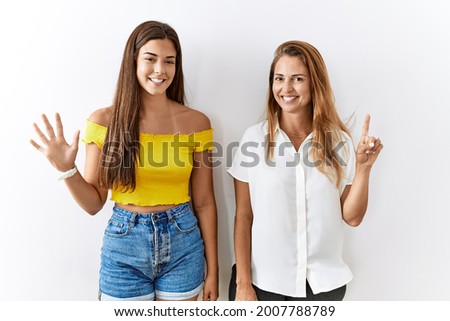 Mother and daughter together standing together over isolated background showing and pointing up with fingers number six while smiling confident and happy. 