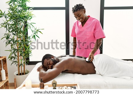 African american man reciving back massage with black stones at beauty center. Royalty-Free Stock Photo #2007798773