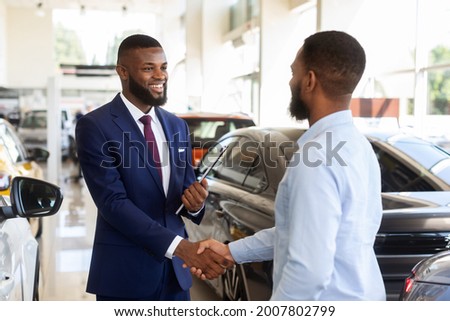 Smiling Car Seller Shaking Hands With Client After Successful Deal, Happy African American Man Buying New Vehicle In Dealership Center, Making Agreement With Salesperson In Modern Auto Showroom Royalty-Free Stock Photo #2007802799