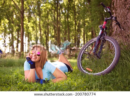 Happy young lady relaxing on a green meadow after cycling