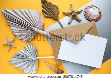mockup invitation card. craft envelope with white blank for text, seashells and exotic leaves on a yellow-gray background 