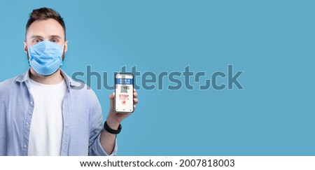 Coronavirus Protection Advert, Stop Covid-19. Portrait of young guy in face mask holding showing cellphone with qr code in hand, isolated on blue studio background, free copy space, banner, panorama