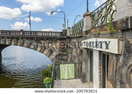 A public restroom entrance under a scenic old bridge in Prague, Czech Republic.