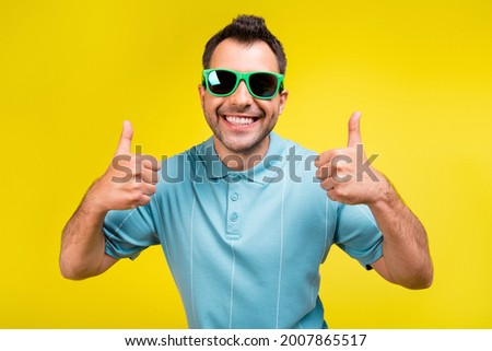 Photo of cool brunet man show thumb up wear spectacles blue t-shirt isolated on yellow color background