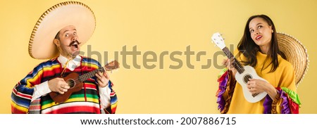 Playing ukulele. Half-size portraits of young couple, man and woman in mexican national clothing and sombrero over yellow background. Collage. Concept of human emotions, facial expression Royalty-Free Stock Photo #2007886715