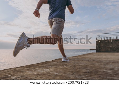 Cropped up photo shot young sporty athletic fit sportsman man in sports clothes shorts warm up training jog run fast at sunrise sun dawn over sea beach outdoor on pier seaside in summer day morning.