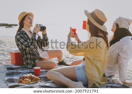 Full length three friends young women in straw hat summer clothes have picnic hang out take photo drink liguor have fun raise toasts outdoors on sea beach background People vacation journey concept