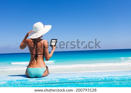 Girl with white hat reads kindle on beach