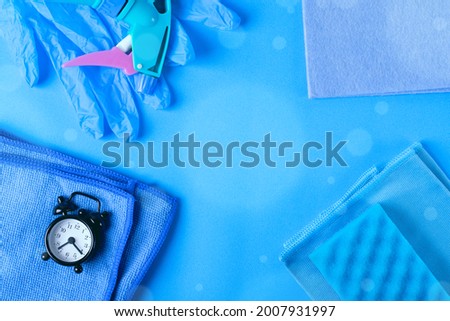 Blue cleaning set. Rags, sponge, spray bottle, latex gloves and alarm clock on blue background. Monochrome flat lay. Business card template with copy space