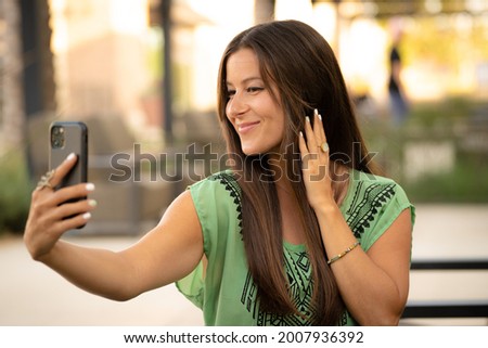 Beautiful Pretty Young Brunette Woman Taking Smiling Funny Selfie Photo Picture with Phone in Natural Soft Daylight at Mall Café Outside