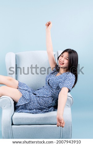 A woman wearing a blue dress, lying slanted on the sofa, stretching and smiling