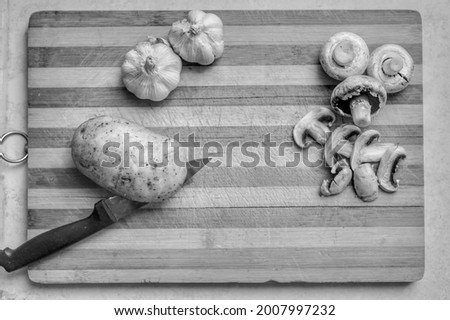 knife cutting potato and some mushrooms in the right of picture and two Garlic plants 