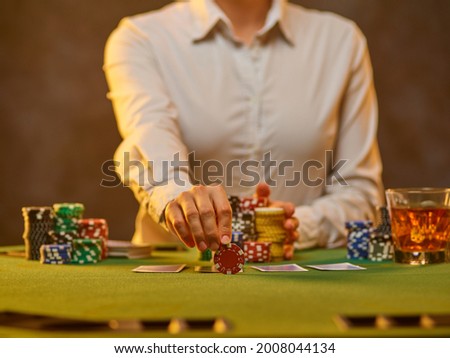 A croupier in a white uniform shirt lays out gambling chips on the table. The cards are on the table. Gambling business, pastime, leisure. Close-up. Brownish green tones. Royalty-Free Stock Photo #2008044134
