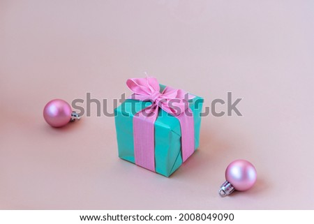Teal blue gift box with pink bow and Christmas balls on beige background.