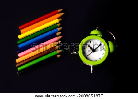 Close-Up Of light green Alarm Clock With Colored Pencils black Background. time to draw. Art school. Selective focus.