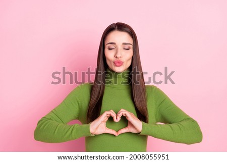 Photo of dreamy young happy woman make fingers heart shape send air kiss isolated on pastel pink color background