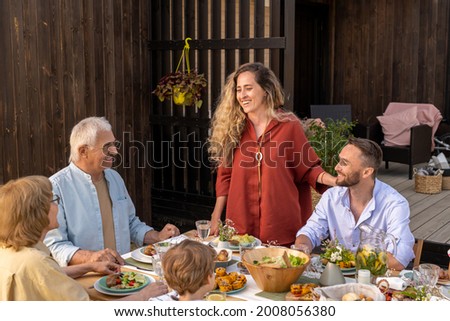 Beautiful young woman with long curly hair giving toast at dinner party with her family Royalty-Free Stock Photo #2008056380
