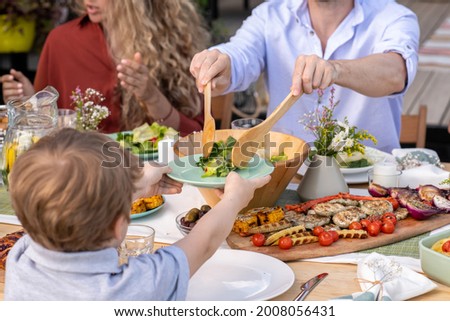 Close-up image of young man putting healthy vegetable salad in plate of his little son