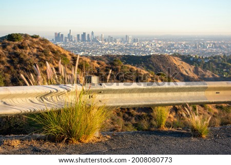 Highway guardrail barrier on road leading to the top of Mount Lee in Santa Monica mountains. Blurred Los Angeles downtown skyscrapers on horizon. Royalty-Free Stock Photo #2008080773