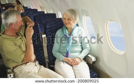 Senior man taking picture of senior woman on airplane
