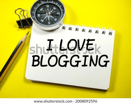 Business concept.Text I LOVE BLOGGING on notebook with paper clips,compass and pencil on a yellow background.