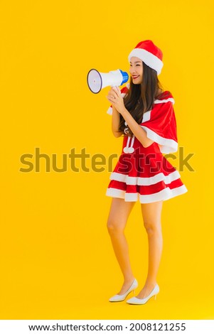 Portrait beautiful young asian woman wear christmas clothes and hat use megaphone on yellow isolated background