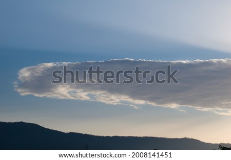 A very long white cloud in blue sky and mountain in background.