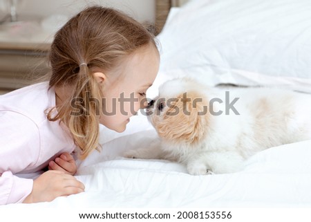 Child with baby dog. Kids play with puppy. Little kid girl and puppy dog on white bed at home. Pet at home. Animal care. Friendship between animal and children