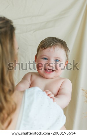 Beautiful young mother with blue-eyed little daughter on a beige background.