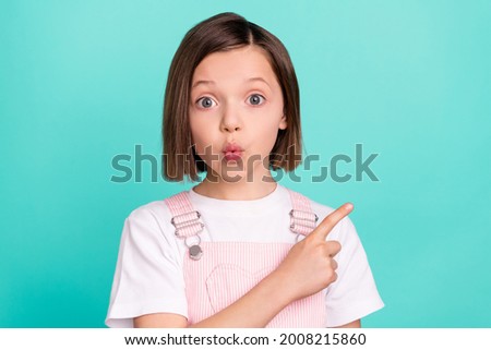 Photo of sweet excited school girl wear pink overall smiling pointing finger empty space isolated teal color background