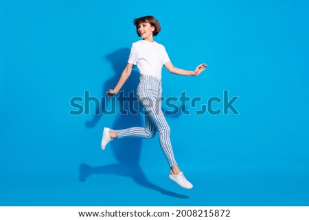 Photo of cute shiny young woman dressed casual clothes running looking back empty space smiling isolated blue color background Royalty-Free Stock Photo #2008215872