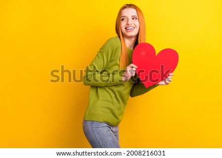 Photo of funky red hairdo young lady hold heart look empty space wear green sweater isolated on yellow color background