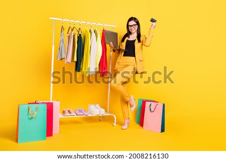 Full size photo of young woman happy smile shop online laptop pay credit card wardrobe bags sale isolated over yellow color background