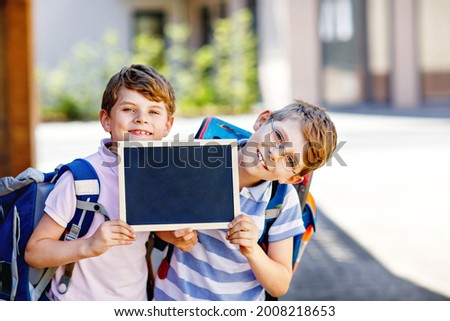 Two little kid boys with backpack or satchel. Schoolkids on the way to school. Healthy children, brothers and best friends outdoors on street leaving home. School's out on chalk desk. Happy siblings. Royalty-Free Stock Photo #2008218653