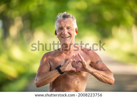 Old but fit man with grey hair shows a heart gesture with his fingers as a sign of his healthy cardiovascular system. Royalty-Free Stock Photo #2008223756